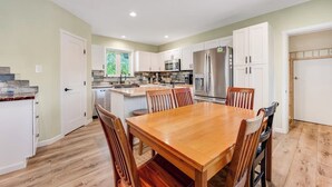 A kitchen with white cabinets, a wooden dining table, and a stainless steel refrigerator. - Two-story dog-friendly getaway with WiFi, wood-burning fireplace, & washer/dryer (Fraser)