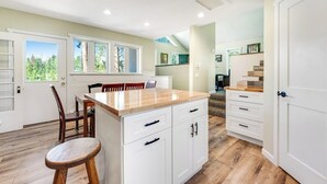 A modern kitchen with white cabinetry, a wooden island, and a dining area with chairs. - Two-story dog-friendly getaway with WiFi, wood-burning fireplace, & washer/dryer (Fraser)