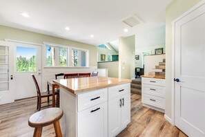A modern kitchen with white cabinetry, a wooden island, and a dining area with chairs. - Two-story dog-friendly getaway with WiFi, wood-burning fireplace, & washer/dryer (Fraser)