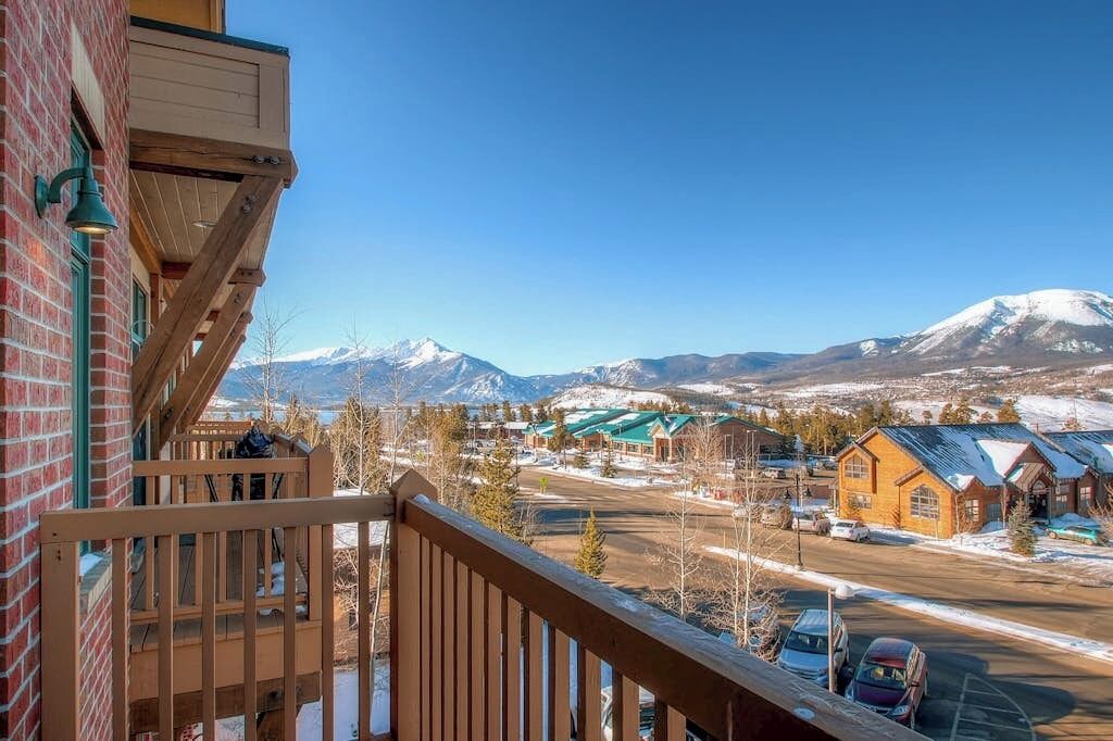 Un balcon avec vue sur des montagnes enneigées, un parking et des bâtiments dotés de toits végétalisés.