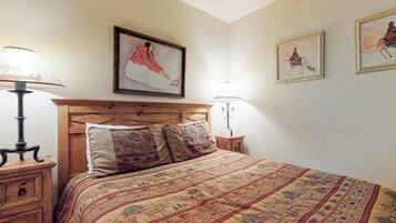 A bedroom with a wooden headboard, a patterned bedspread, two bedside lamps, and framed artwork on the wall.