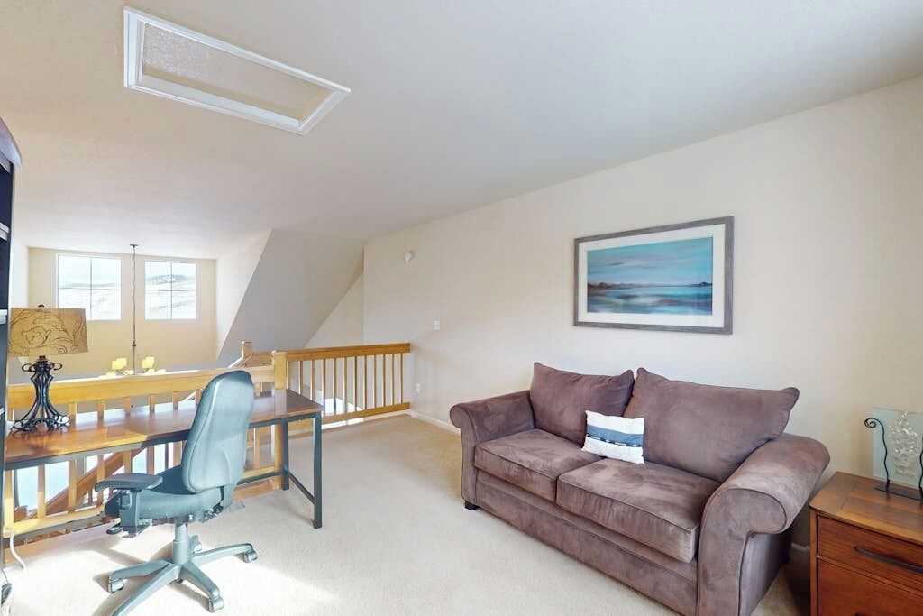 A room with a desk, office chair, couch, and a painting on the wall.