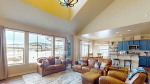 A spacious living room with leather sofas, a coffee table, and a large window offering a view of a snowy landscape. - Getaway with fireplace, gas fire pit, shared pool/hot tub-minutes to ski & golf (Granby)