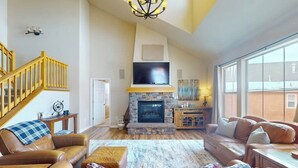 A spacious living room with a fireplace, leather sofas, a TV, and a staircase. - Getaway with fireplace, gas fire pit, shared pool/hot tub-minutes to ski & golf (Granby)