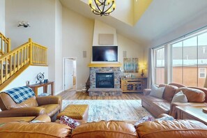 Ein geräumiges Wohnzimmer mit Kamin, Ledersofas, Fernseher und einer Treppe.