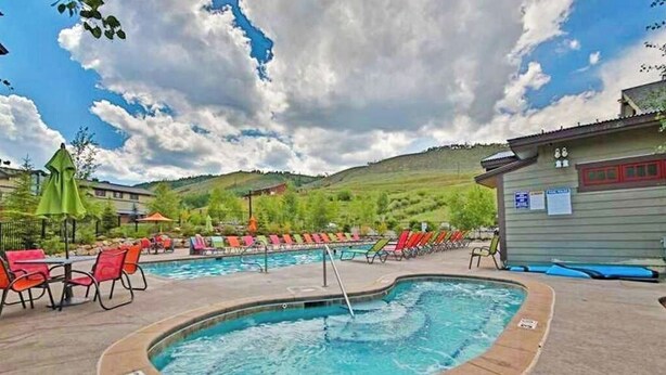 A pool area with multiple pools, lounge chairs, and a building with signage. - Getaway with fireplace, gas fire pit, shared pool/hot tub-minutes to ski & golf (Granby)