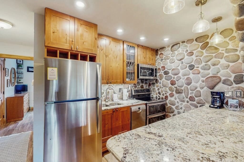 Una cocina con armarios de madera, un refrigerador de acero inoxidable, un microondas y una pared de piedra.