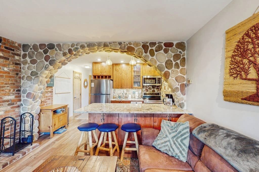 Une cuisine chaleureuse avec une arche en pierre, des armoires en bois et un coin bar avec des tabourets.