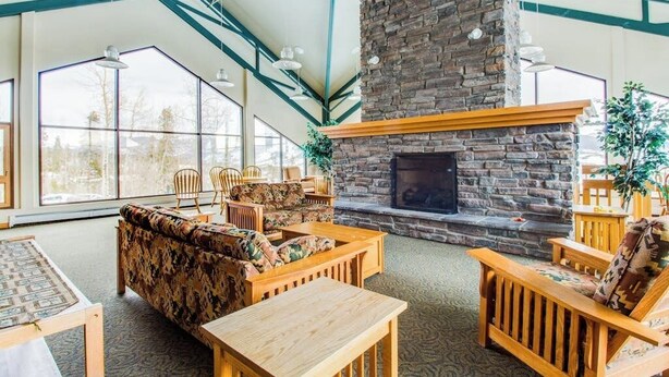 A spacious room with a stone fireplace, wooden furniture, and large windows. - Conveniently Located Condo with Pool, Hot Tub & Sauna - Near Slopes & Lake (Silverthorne)