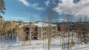 A building with a snow-covered roof, surrounded by trees and mountains in the background. - Conveniently Located Condo with Pool, Hot Tub & Sauna - Near Slopes & Lake (Silverthorne)