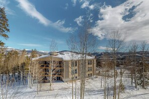 A building with a snow-covered roof, surrounded by trees and mountains in the background. - Conveniently Located Condo with Pool, Hot Tub & Sauna - Near Slopes & Lake (Silverthorne)