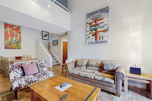 Ein geräumiges Wohnzimmer mit hoher Decke, einer Treppe, einem Essbereich und einem Poster von Steamboat Springs in Colorado.