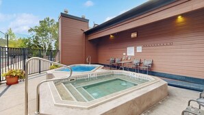 Ett bubbelbad och en utomhusplats med sittmöbler och en pool, omgivet av en trävägg och ett metallstaket.