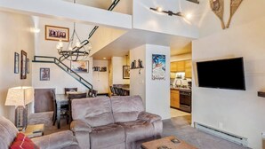 Een woonkamer met een bank, salontafel en een aan de muur bevestigde televisie.