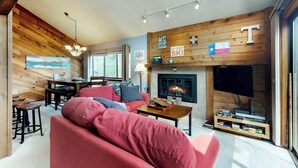 A cozy living room with a fireplace, a television, and a wooden wall. - Spacious lodge-style duplex with private hot tub - near hiking, skiing, & more (Silverthorne)