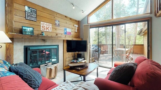 A cozy living room with a fireplace, a television, and a large sliding glass door leading to an outdoor area. - Spacious lodge-style duplex with private hot tub - near hiking, skiing, & more (Silverthorne)
