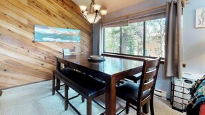 A wooden-paneled room with a dining table, chairs, a chandelier, a painting, and a window with curtains. - Spacious lodge-style duplex with private hot tub - near hiking, skiing, & more (Silverthorne)