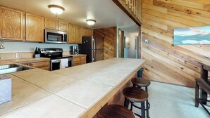 A kitchen with wooden cabinets, a microwave, a stove, and a large island with bar stools. - Spacious lodge-style duplex with private hot tub - near hiking, skiing, & more (Silverthorne)