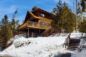 Eine Holzhütte mit Balkon, Treppe und verschneiter Landschaft.