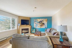 Ein Wohnzimmer mit Kamin, Fernseher, Sofa, Couchtisch und einem Bild an der Wand.