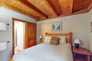A bedroom with a wooden ceiling, a bed with white bedding, two bedside tables with lamps, and a painting on the wall. - Wildernest condo with sauna and tennis, 5 miles to Lake Dillon (Silverthorne)