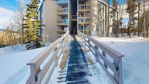 Lumipeitteinen polku johtaa rakennukseen, jossa on parvekkeita ja puinen aita.