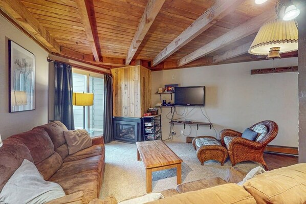 A cozy living room with a wooden ceiling, a sofa, a coffee table, a TV, and a fireplace. - Wildernest condo with sauna and tennis, 5 miles to Lake Dillon (Silverthorne)