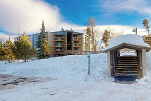 A snow-covered outdoor area with a building entrance, a staircase, and a sign indicating a parking area. - Wildernest condo with sauna and tennis, 5 miles to Lake Dillon (Silverthorne)
