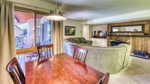 A dining area with a wooden table and chairs, a sofa, and a television. - Cozy condo w/ private balcony, shared pool, & hot tub - close to golf & slopes (Keystone)