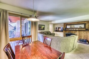 A dining area with a wooden table and chairs, a sofa, and a television. - Cozy condo w/ private balcony, shared pool, & hot tub - close to golf & slopes (Keystone)