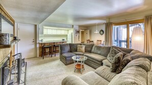 A living room with a sectional sofa, a glass coffee table, and a kitchen area in the background. - Cozy condo w/ private balcony, shared pool, & hot tub - close to golf & slopes (Keystone)