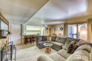 A living room with a sectional sofa, a glass coffee table, and a kitchen area in the background. - Cozy condo w/ private balcony, shared pool, & hot tub - close to golf & slopes (Keystone)