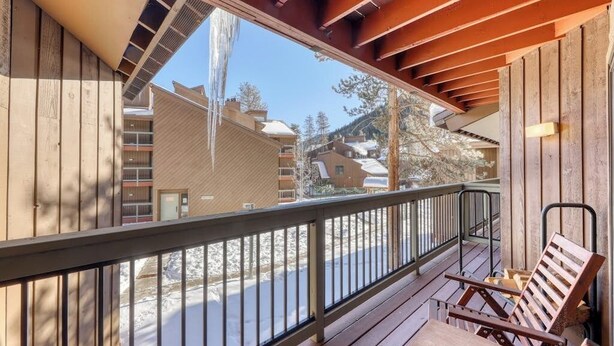 A wooden deck with a railing, wooden benches, and a view of buildings and trees. - Cozy condo w/ private balcony, shared pool, & hot tub - close to golf & slopes (Keystone)