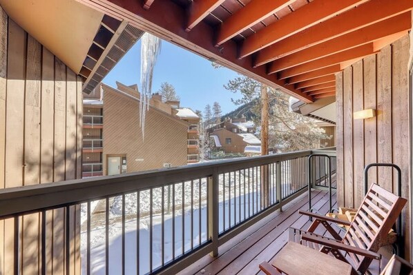 A wooden deck with a railing, wooden benches, and a view of buildings and trees. - Cozy condo w/ private balcony, shared pool, & hot tub - close to golf & slopes (Keystone)