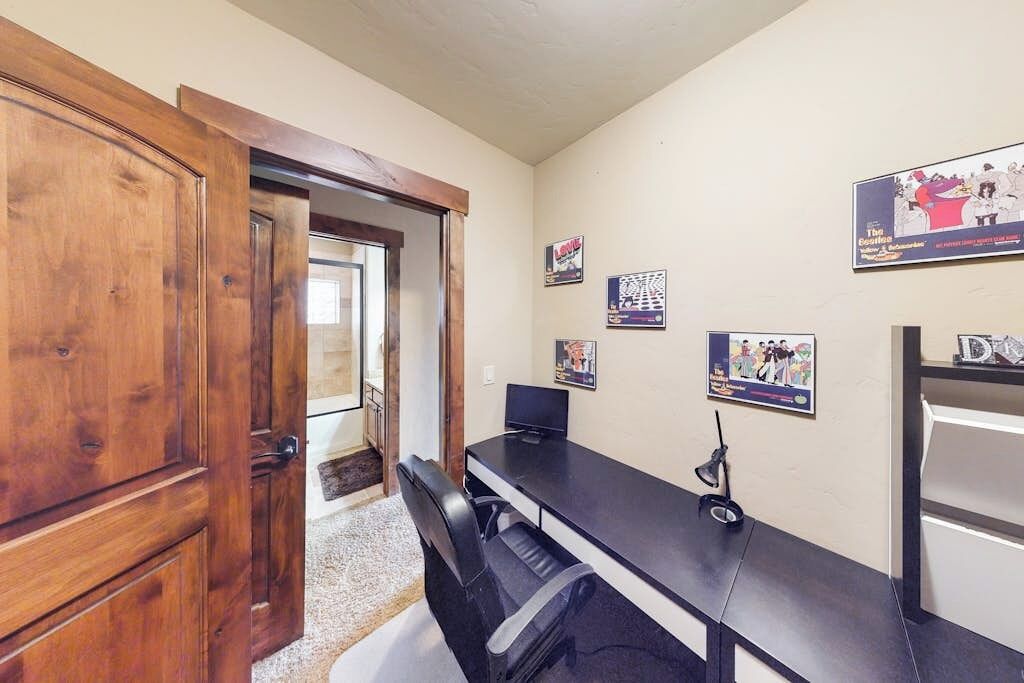 A room with a wooden door, a black desk, and wall-mounted posters.