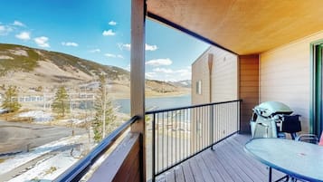 Un balcón con vistas a un lago y montañas, una parrilla y una mesa.