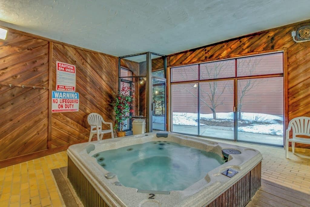 Un jacuzzi en una cabaña de madera con un letrero de advertencia, dos sillas y vistas a un paisaje nevado.