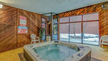 Un jacuzzi en una cabaña de madera con un letrero de advertencia, dos sillas y vistas a un paisaje nevado.