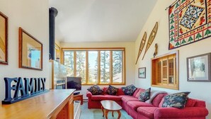 Ett vardagsrum med en röd soffa, ett soffbord i trä och en tv. Det finns stora fönster och en öppen spis.