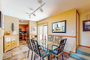 A dining area with a glass table and chairs, a kitchen in the background, and a staircase leading to another level. - Bright home with fireplace & perfect location steps to hiking trails (Dillon)