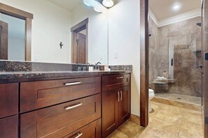 A bathroom with a large mirror, dark wooden cabinets, a glass shower enclosure, and a toilet.