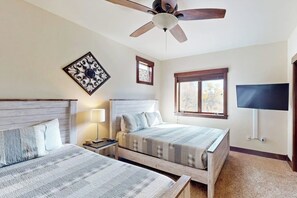 A bedroom with two beds, a ceiling fan, a TV, and a window with blinds.