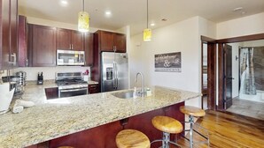 Una cocina moderna con encimeras de granito, electrodomésticos de acero inoxidable y taburetes de madera.