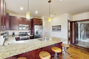 A modern kitchen with granite countertops, stainless steel appliances, and wooden stools. - End-Unit Condo w/Beautiful Blue River & Mountain Views, Free WiFi, & Deck (Silverthorne)