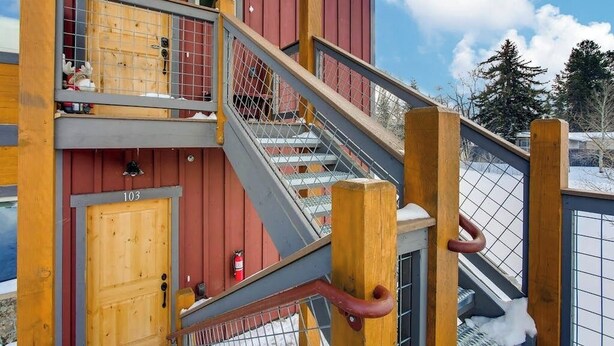 Un edificio de varios pisos con fachada de madera, una escalera con barandillas metálicas y un extintor visible en el interior.