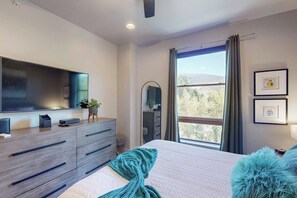 Ein Schlafzimmer mit Bett, Kommode, Fernseher, Fenster mit Blick und Spiegel.