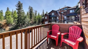 A wooden deck with two red chairs, a view of a forested area, and a multi-story building in the background. - Mountain family townhome w/ fireplace, private balcony & beautiful views (Silverthorne)