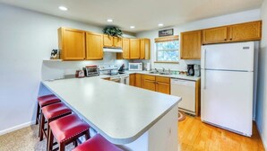 A kitchen with wooden cabinets, a white island with red stools, a white refrigerator, and a window with a view. - Mountain family townhome w/ fireplace, private balcony & beautiful views (Silverthorne)