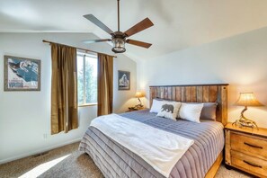 Ein Schlafzimmer mit einem Bett, einem Deckenventilator, einem Nachttisch mit Lampe und zwei Bildern an der Wand.