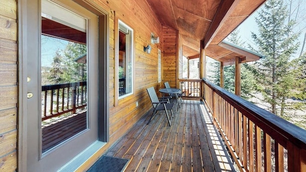 Une terrasse en bois avec une table et des chaises, une porte avec des panneaux de verre et une vue sur les arbres.